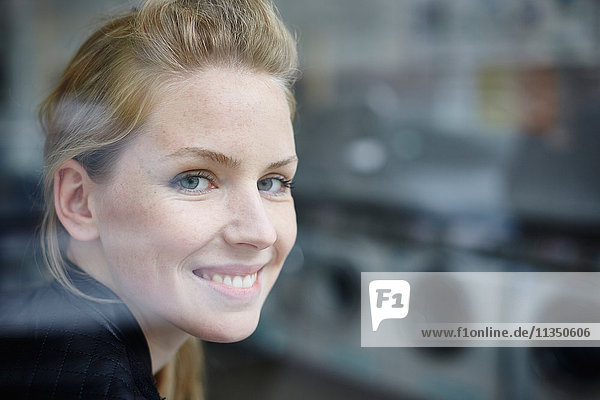 Portrait of smiling young woman behind window pane