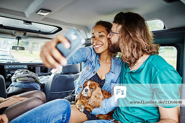 Happy couple with dog taking a selfie in car