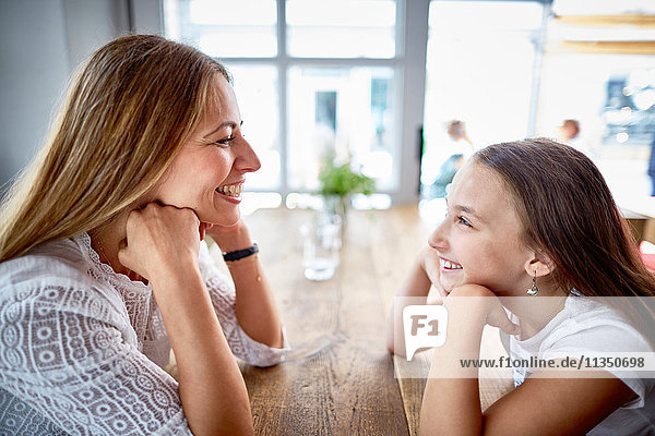 Happy mother and daughter sitting face to face in a restaurant