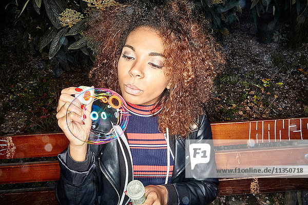 Young woman on park bench blowing soap bubbles