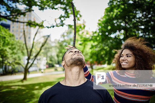 Junger Mann mit seiner Freundin im Park balanciert einen Stock auf seinem Kopf