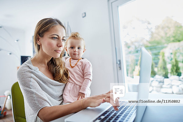 Mutter mit Baby benutzt einen Laptop Zuhause
