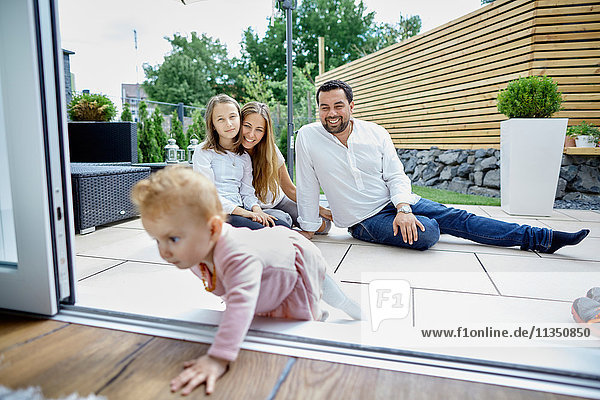 Familie auf der Terrasse schaut zu krabbelndem Baby