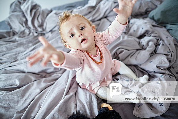 Baby girl in bedroom reaching out her arms