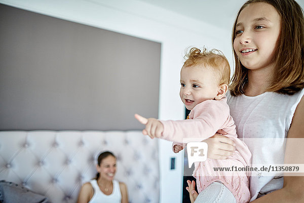 Mädchen trägt ein Baby mit Mutter im Hintergrund