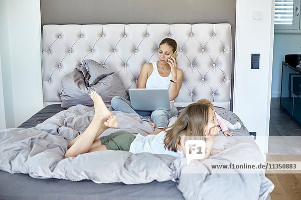 Mutter mit Laptop und Tochter und Baby im Bett