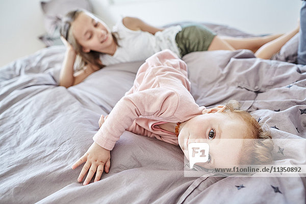 Baby liegt mit ihrer Schwester im Bett