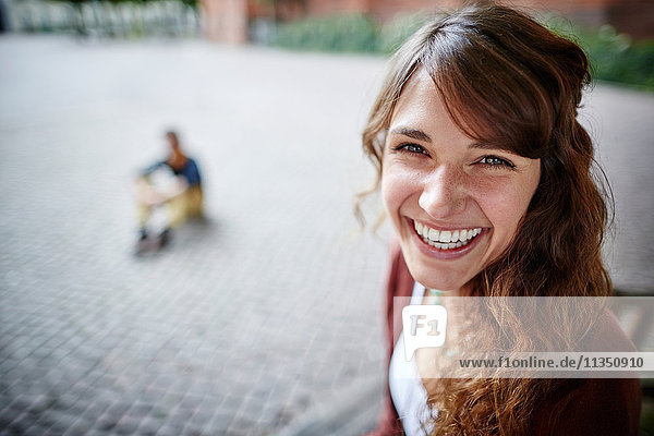 Portrait einer fröhlichen jungen Frau mit Mann im Hintergrund