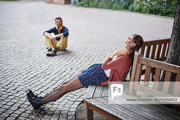 Fröhliche junge Frau sitzt auf einer Bank auf einem Platz