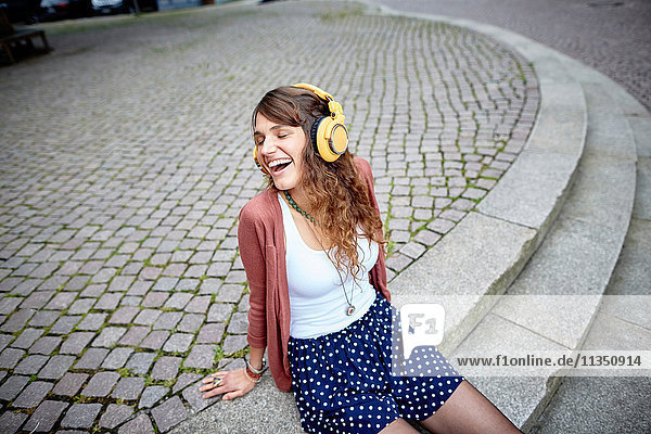 Fröhliche junge Frau sitzt auf einem Platz und hört Musik