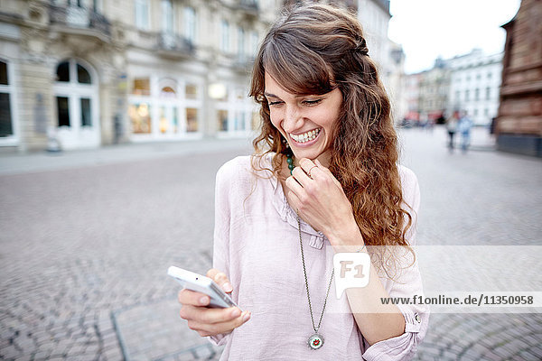 Fröhliche junge Frau in der Stadt schaut auf ihr Handy