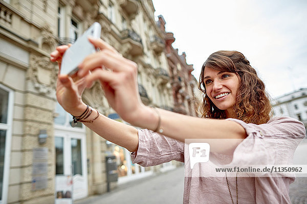 Lächelnde junge Frau in der Stadt macht ein Selfie