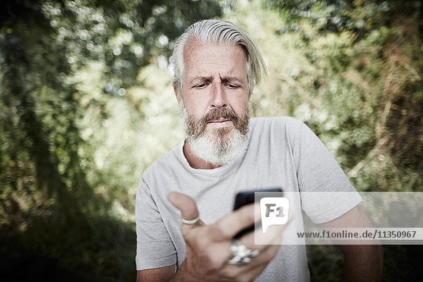 Reifer Mann mit Vollbart im Freien schaut auf Handy