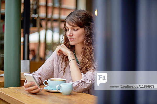 Junge Frau in einem Cafe schaut auf ihr Handy
