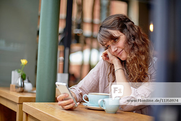 Junge Frau in einem Cafe schaut auf ihr Handy