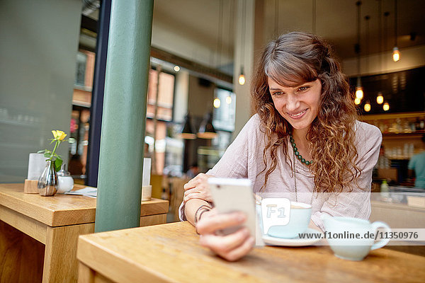 Smiling young woman in a cafe looking at cell phone