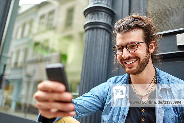 Lächelnder junger Mann schaut auf sein Handy