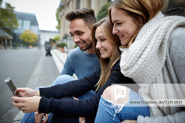 Drei lächelnde Freunde schauen zusammen auf ein Handy