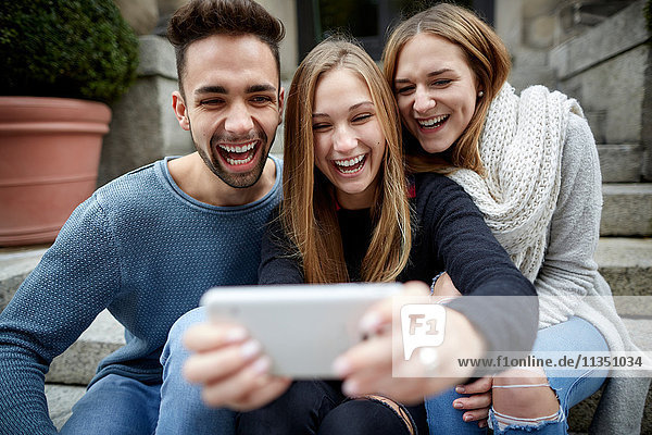 Drei lachende Freunde schauen zusammen auf ein Handy
