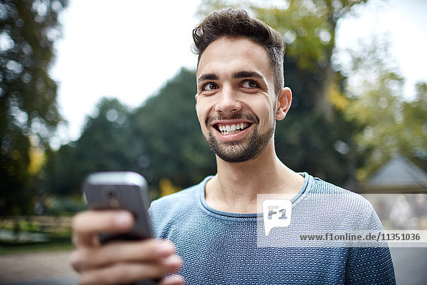 Portrait eines lächelnden jungen Mannes mit Handy im Freien