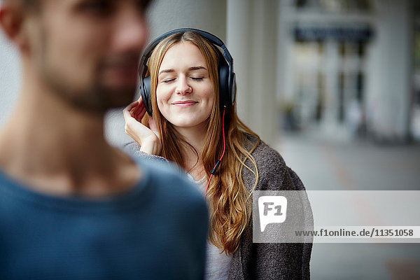 Young woman wearing headphones outdoors with man in foreground