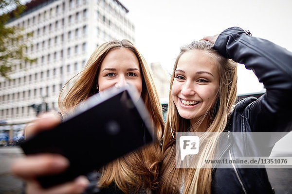 Two happy young women with cell phone outdoors
