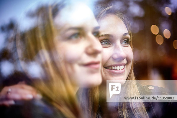 Zwei lächelnde junge Frauen schauen durchs Fenster