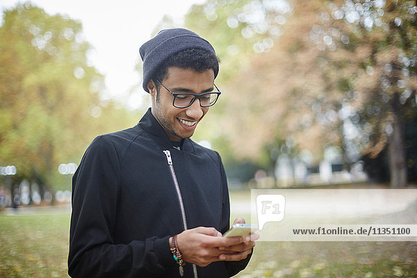 Junger Mann im Park schaut auf sein Handy