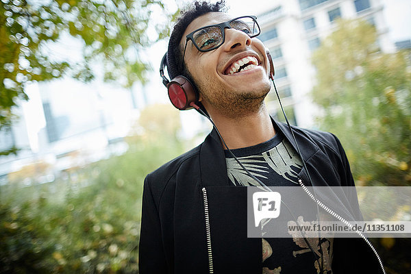 Fröhlicher junger Mann mit Kopfhörern im Park