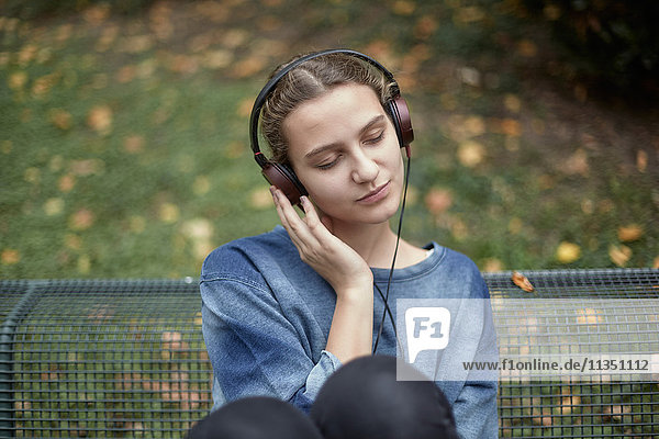 Junge Frau mit geschlossenen Augen und Kopfhörern auf einer Parkbank