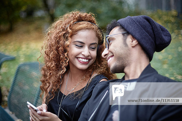 Lächelndes junges Paar mit Handy auf einer Parkbank
