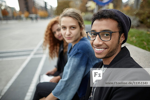 Drei lächelnde Freunde sitzen zusammen im Freien