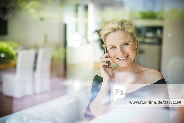 Lächelnde reife Frau telefoniert hinter Fenster