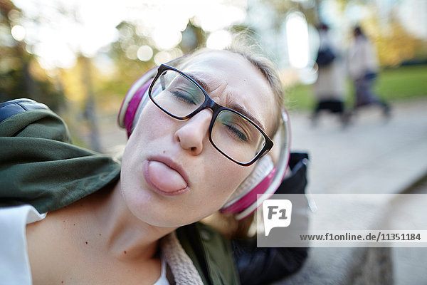 Frau mit Kopfhörern im Freien streckt die Zunge heraus