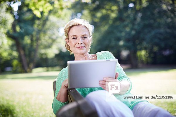Reife Frau benutzt einen Tablet-PC auf der Parkbank