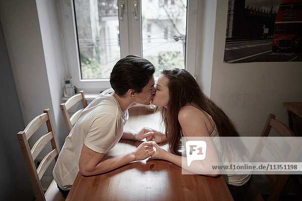 Young couple in love sitting on table at home kissing