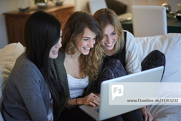 Three happy women sitting on couch looking at laptop together