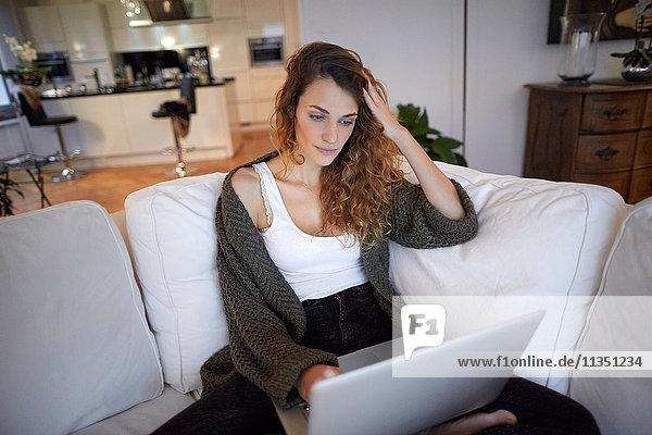 Frau sitzt auf der Couch und schaut auf ihren Laptop