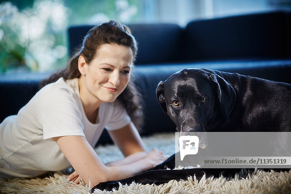Frau liegt mit Hund auf dem Teppich