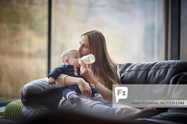 Mother bottle feeding baby on couch