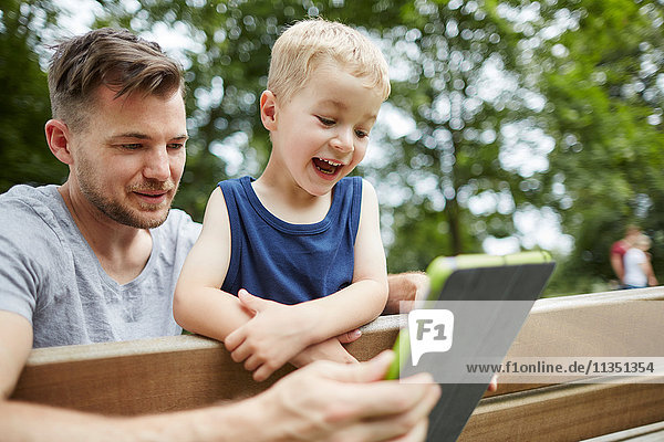 Vater und fröhlicher Sohn schauen auf Tablet