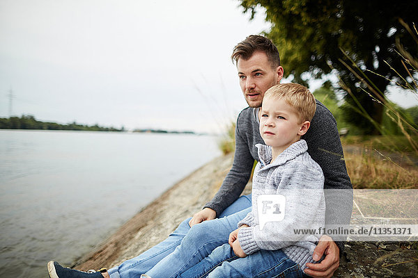 Vater und Sohn sitzen am Flussufer