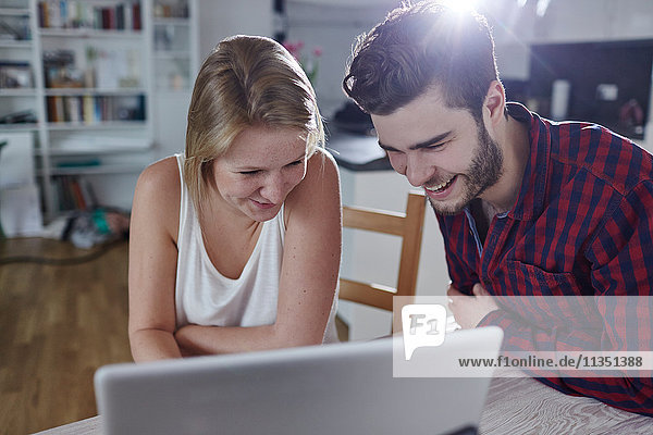 Fröhliches junges Paar Zuhause schaut auf einen Laptop
