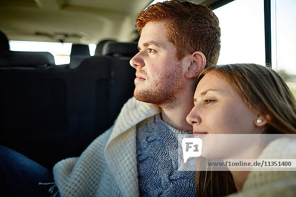 Young couple inside car wrapped in a blanket