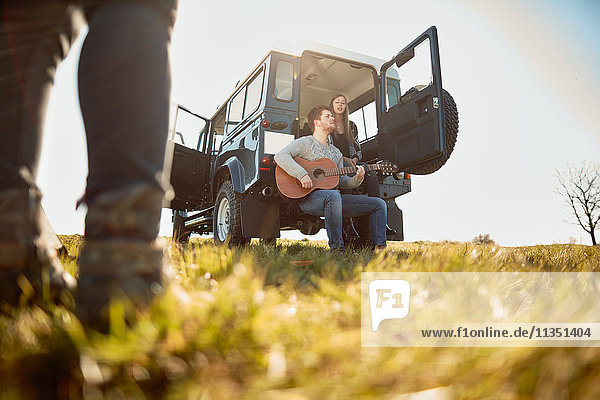Young couple with off-road vehicle on meadow making music