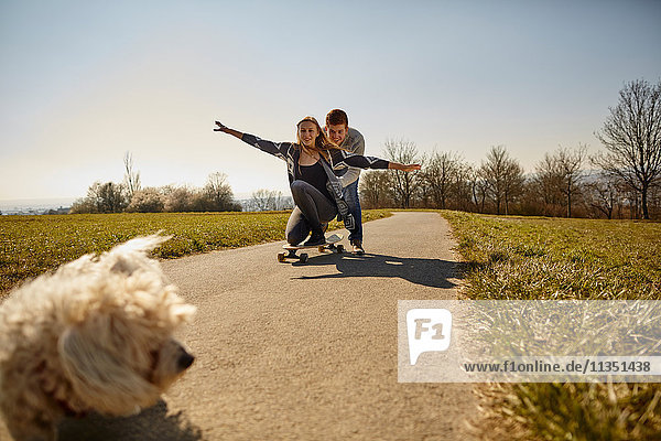 Hund und junges Paar mit Skateboard auf einem Feldweg