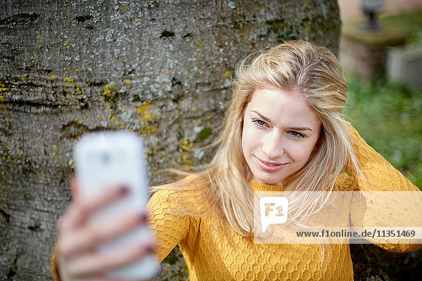 Junge Frau an einem Baumstamm macht ein Selfie