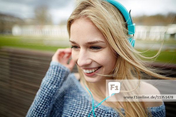 Glückliche junge Frau mit Kopfhörern auf einer Bank