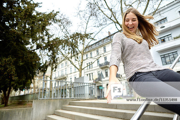 Exuberant young woman sliding on handrail