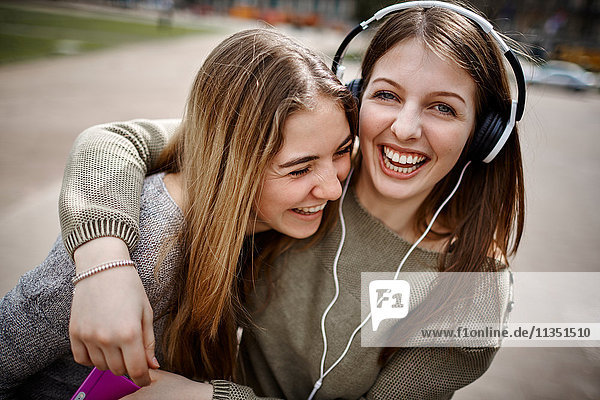 Glückliche junge Frau mit Freundin trägt Kopfhörer